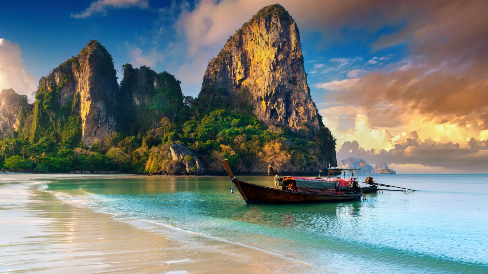 Longtail boat on Railay Beach at sunrise below limestone cliffs in Krabi, Thailand