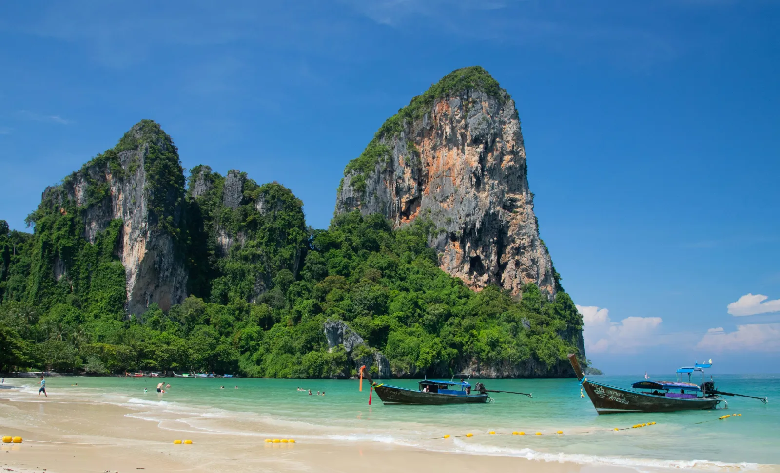 Longtail boats moored on Railay Beach beneath a huge limestone rock formation in Krabi