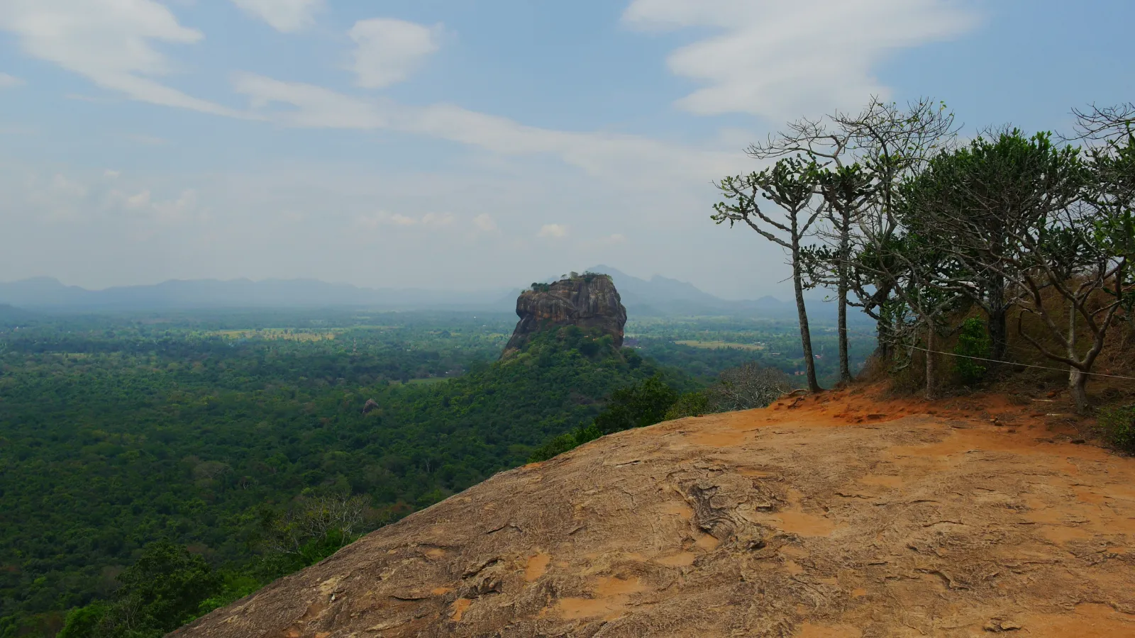 Sigiriya Lion Rock seen across the forest from a neighbouring rocky hilltop viewpoint