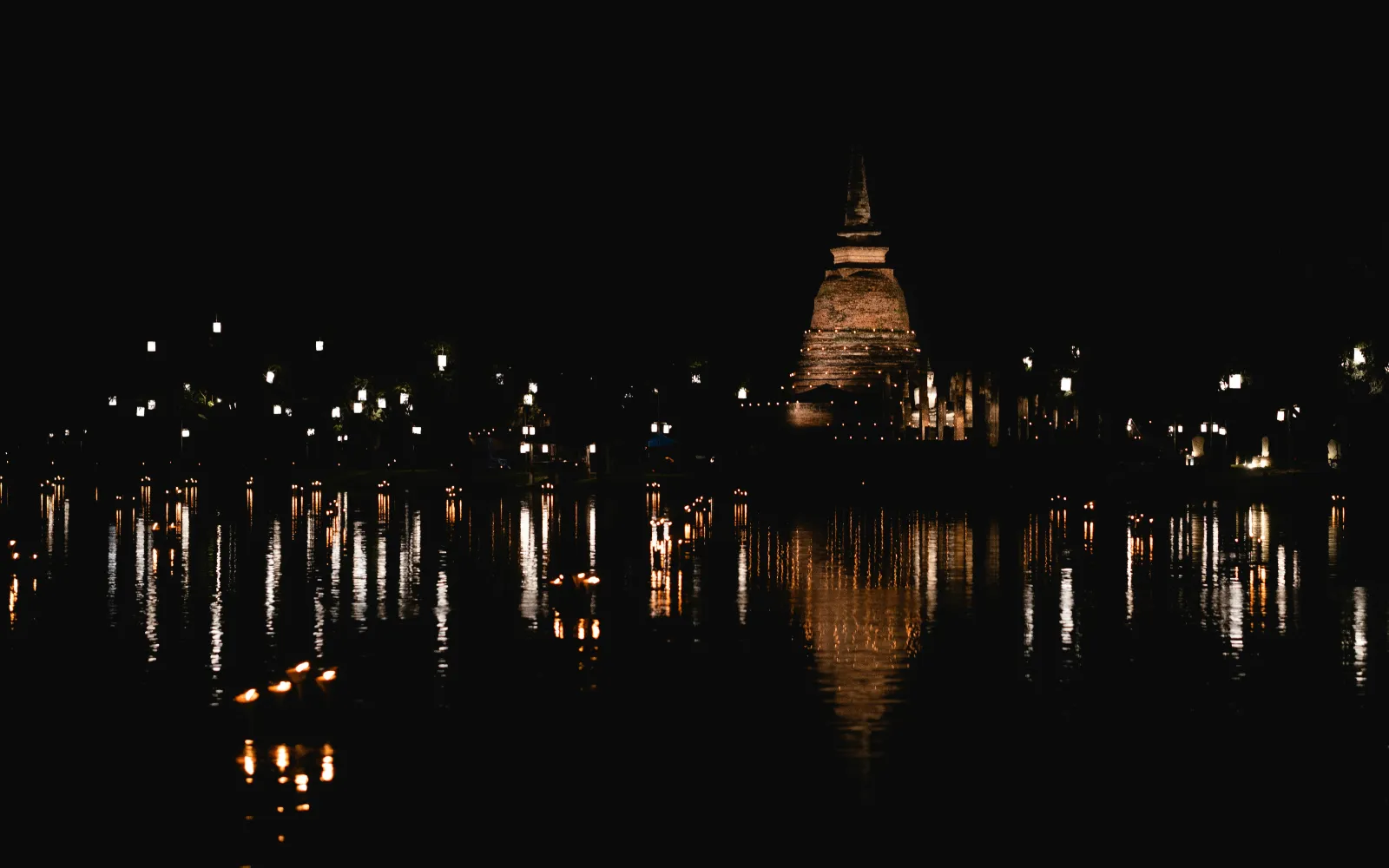 Ancient chedi reflected in a pond at Sukhothai Historical Park during Loy Krathong night
