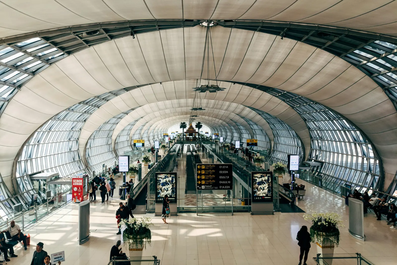 Long curved glass concourse of Suvarnabhumi Airport in Bangkok with walking travellers