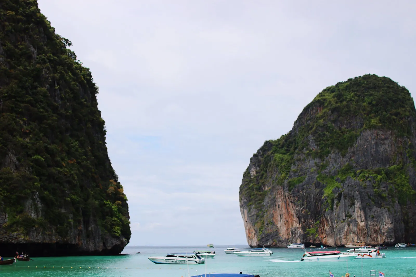 Speedboats anchored between tall limestone cliffs in clear water off a southern Thai island