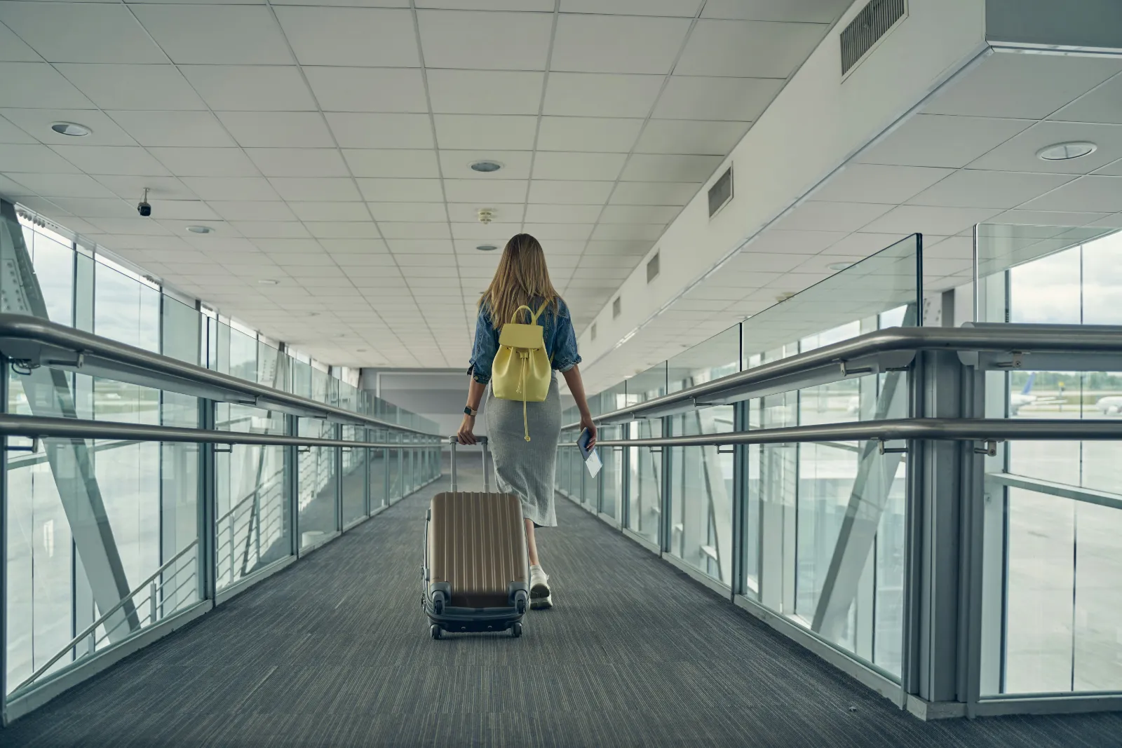 Traveller pulling a suitcase through a bright glass airport corridor after landing