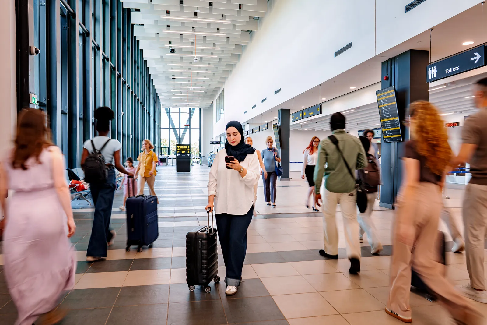 Travellers with suitcases walking through a busy airport terminal hall after landing