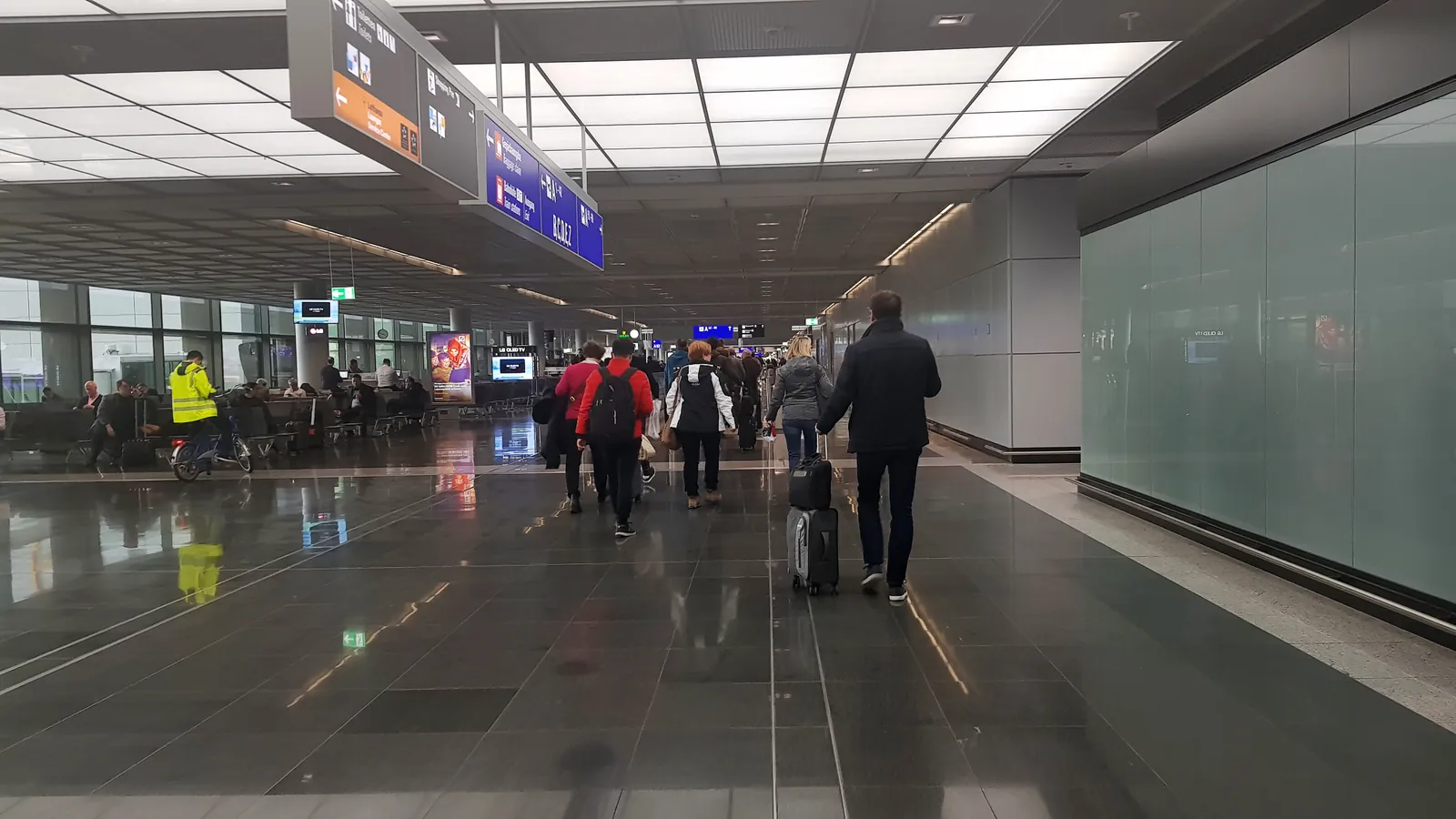 Travellers with luggage walking along a wide, bright airport terminal corridor