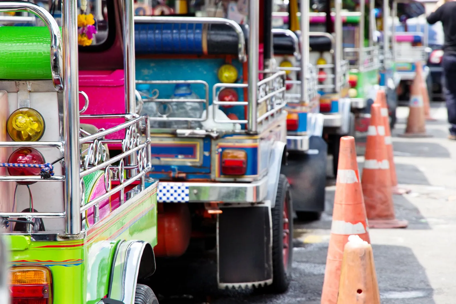 Colourful tuk tuk taxis lined up beside traffic cones on a busy Bangkok street