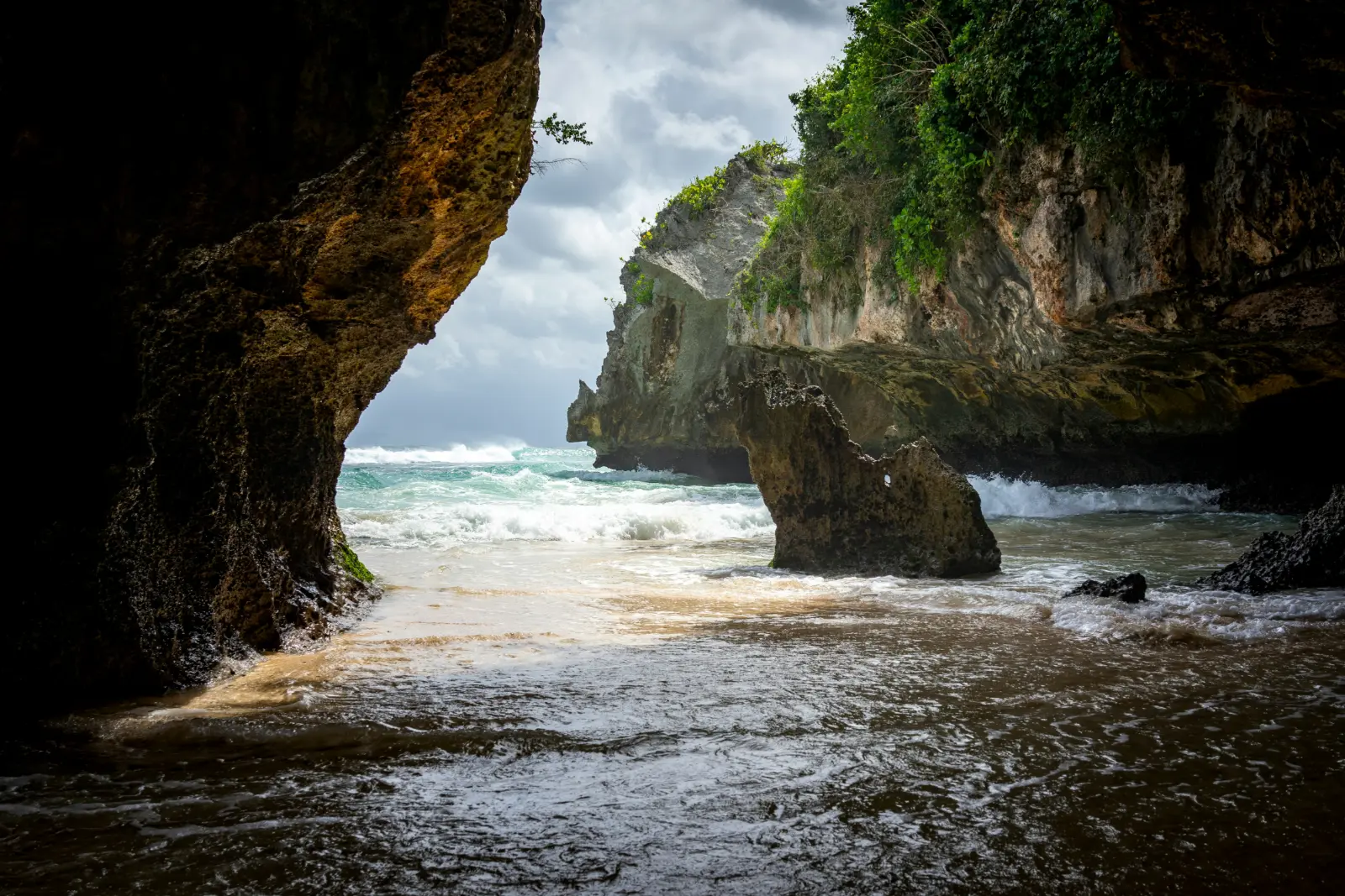 Surf rolling onto a hidden beach below the limestone cliffs of Uluwatu in southern Bali