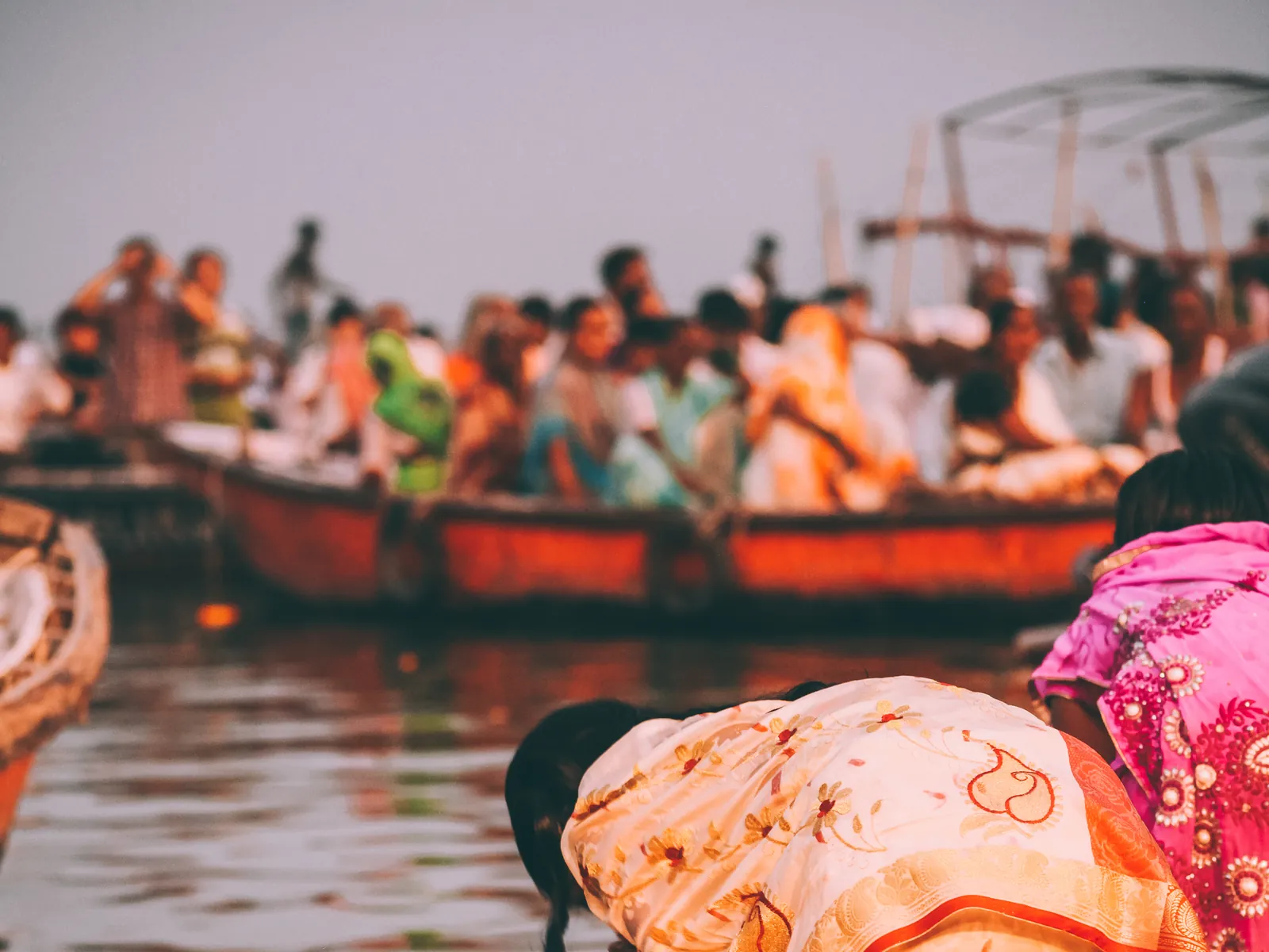 Pilgrims in wooden boats and a woman in a sari praying at the edge of the Ganges at dawn in Varanasi