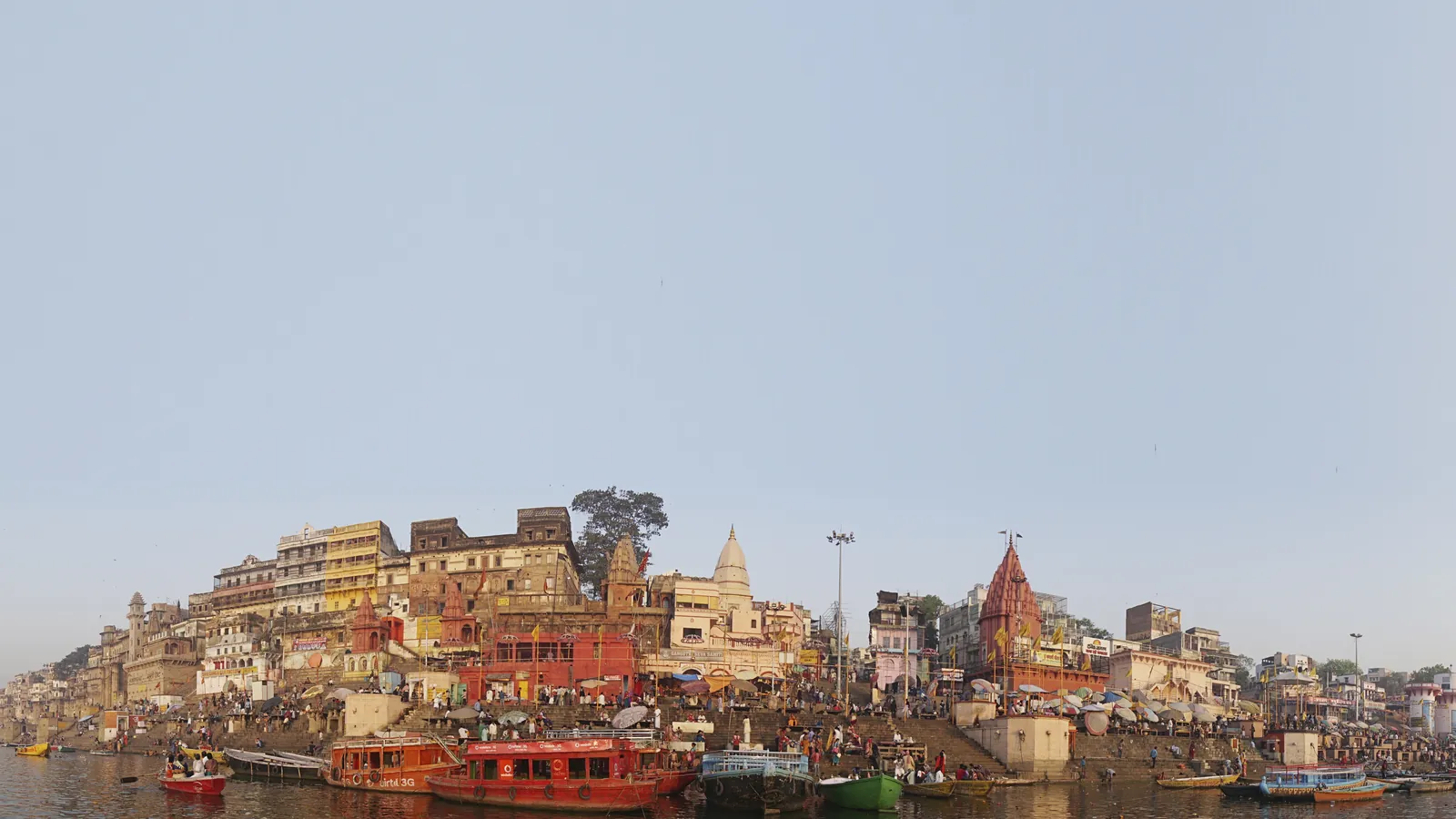 Varanasi ghats, temples and moored boats seen from the Ganges river on a clear morning