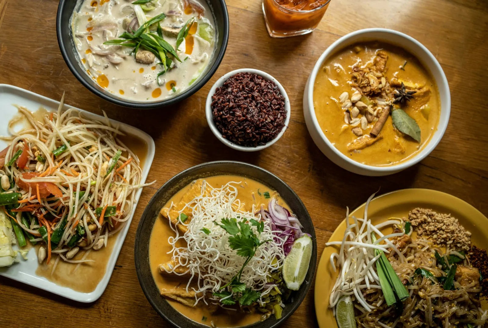 Table of vegan Thai dishes including curry, papaya salad, noodles and purple rice