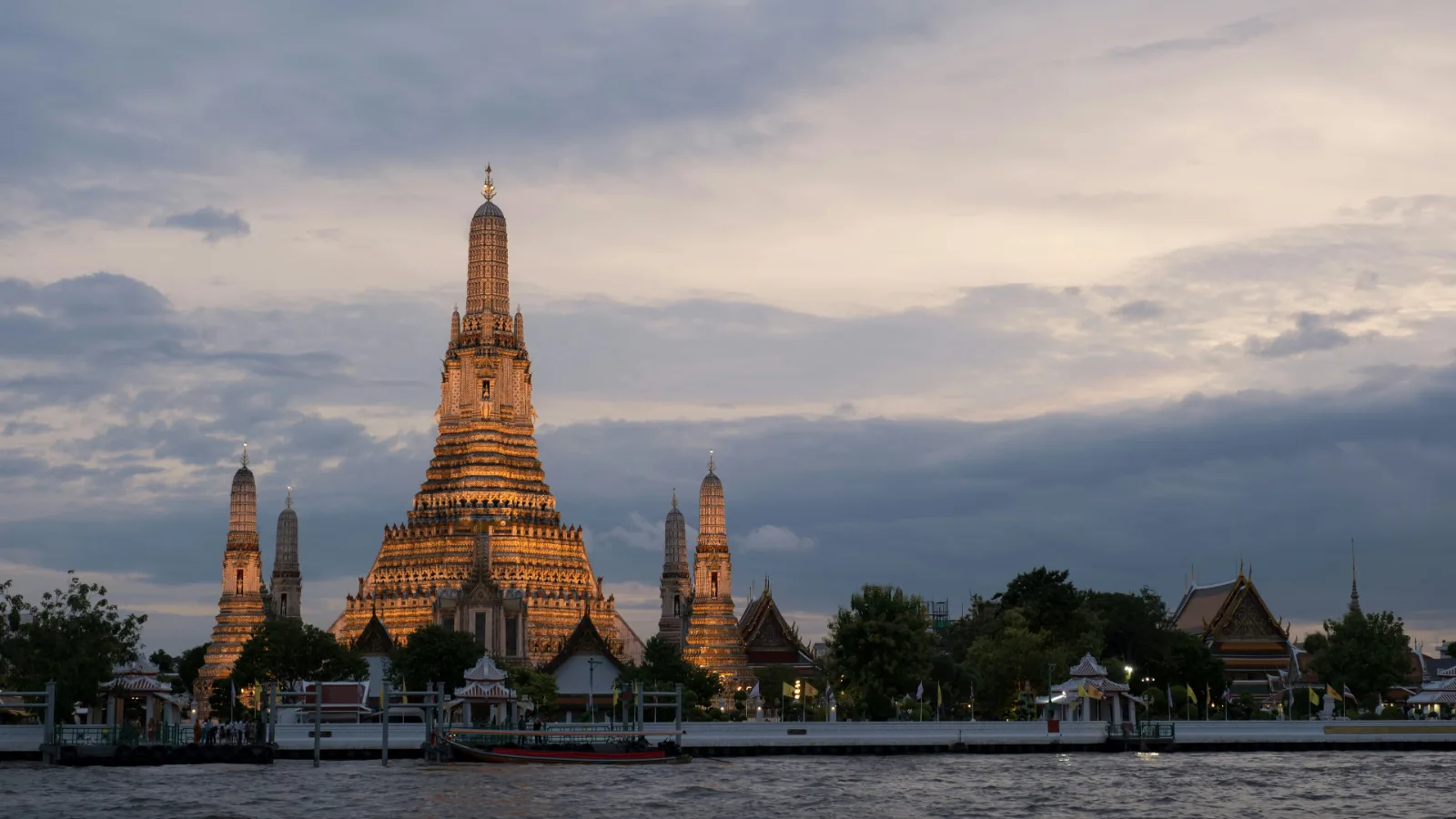 Wat Arun temple spires beside the Chao Phraya River in Bangkok at sunset