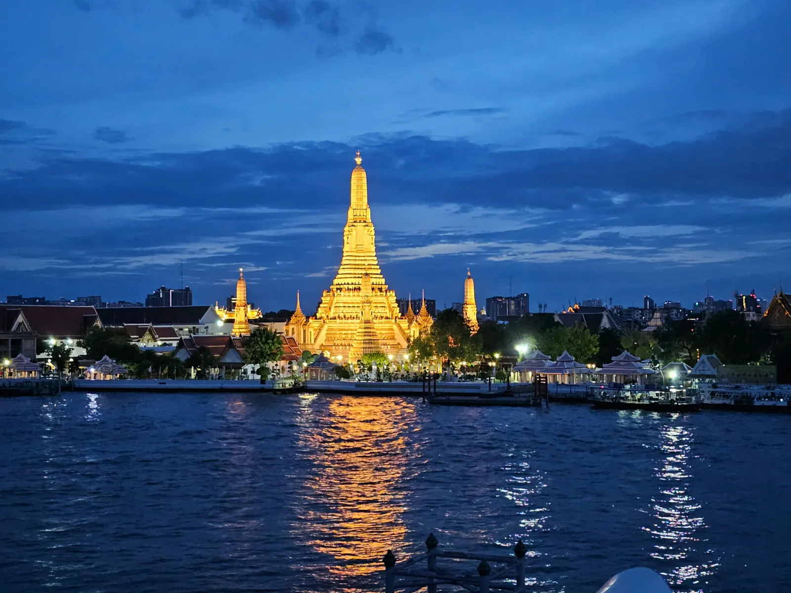 Wat Arun temple lit up beside the Chao Phraya River in Bangkok at dusk